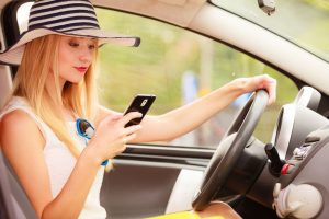 Distracted driver. Young attractive woman using mobile phone texting or read message while driving the car.
